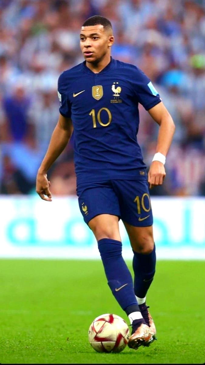 A male soccer player in a blue France national team uniform, number 10, is running on the field with the ball at his feet during a match, while fans watching via Ecuador IPTV enjoy the action with a blurred crowd in the background.