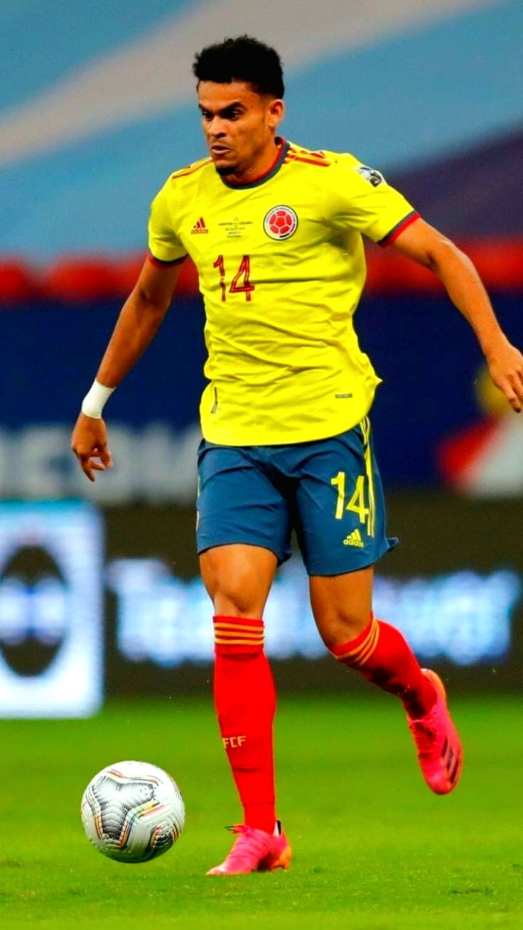 A male soccer player wearing a yellow Colombia national team jersey with number 14, blue shorts, and red socks dribbles a ball on the field during a match, captured live on Ecuador IPTV.